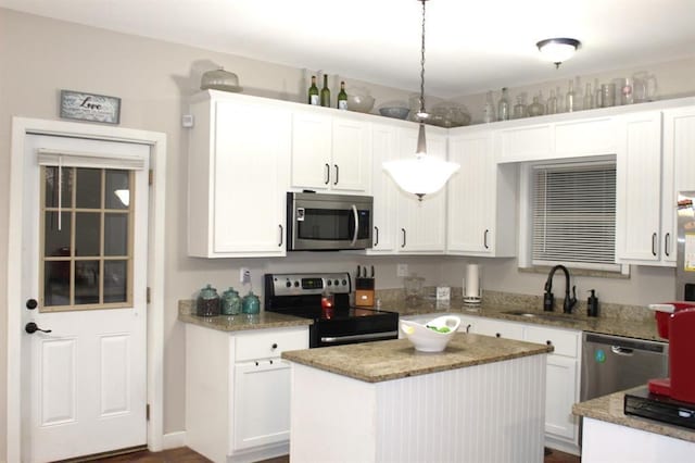 kitchen featuring light stone countertops, stainless steel appliances, a sink, white cabinets, and a center island