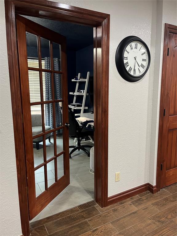 hall with dark wood-style flooring, a textured wall, baseboards, and french doors