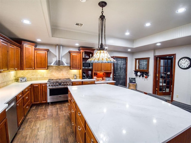 kitchen with visible vents, brown cabinetry, appliances with stainless steel finishes, decorative light fixtures, and wall chimney range hood