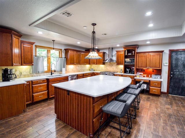 kitchen featuring wall chimney exhaust hood, a center island, stainless steel appliances, light countertops, and a sink