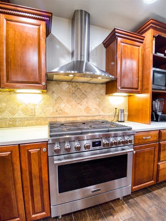 kitchen with high end stainless steel range oven, decorative backsplash, light countertops, and wall chimney range hood