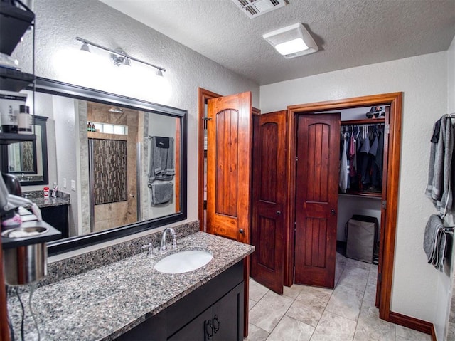 bathroom with a textured ceiling, a textured wall, vanity, visible vents, and a walk in closet