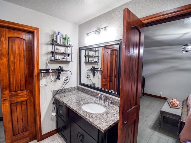 bathroom featuring vanity, baseboards, a textured ceiling, and a textured wall