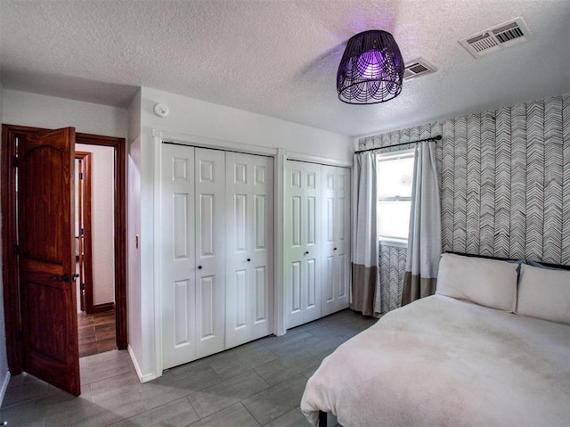 bedroom with a textured ceiling, two closets, visible vents, and baseboards