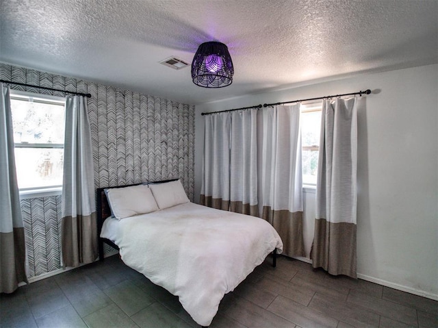 bedroom with visible vents, a textured ceiling, baseboards, and multiple windows