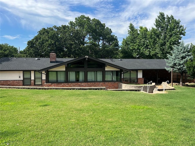 view of front of home featuring brick siding, a shingled roof, a front lawn, a chimney, and a patio area