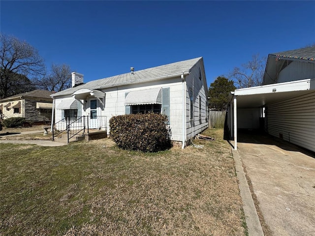 back of house featuring a carport, a chimney, concrete driveway, and a lawn