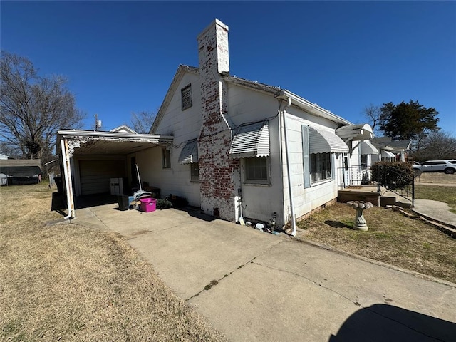 view of side of property featuring driveway, a chimney, and a carport