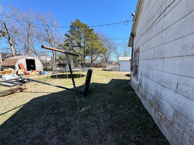 view of yard featuring a trampoline, an outbuilding, fence, and a storage shed