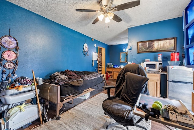 bedroom with a textured ceiling, ceiling fan, wood finished floors, and freestanding refrigerator