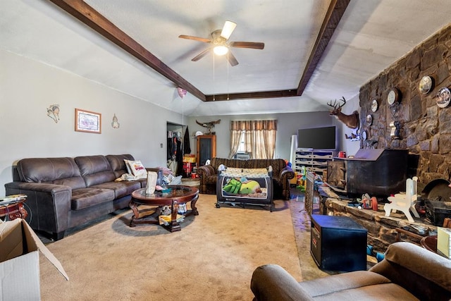 living room featuring a raised ceiling, a ceiling fan, light colored carpet, a wood stove, and beam ceiling