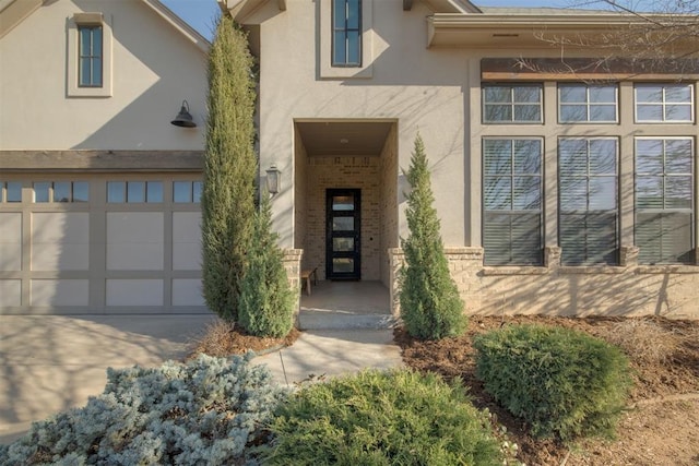 view of exterior entry with stucco siding, a garage, and concrete driveway