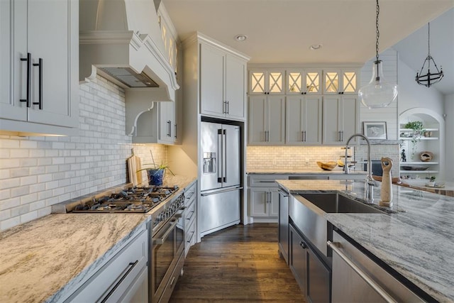 kitchen with light stone counters, premium appliances, dark wood-style floors, custom exhaust hood, and a sink