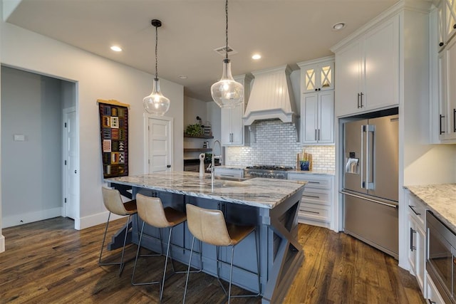 kitchen with dark wood-style floors, stainless steel appliances, custom range hood, white cabinetry, and backsplash