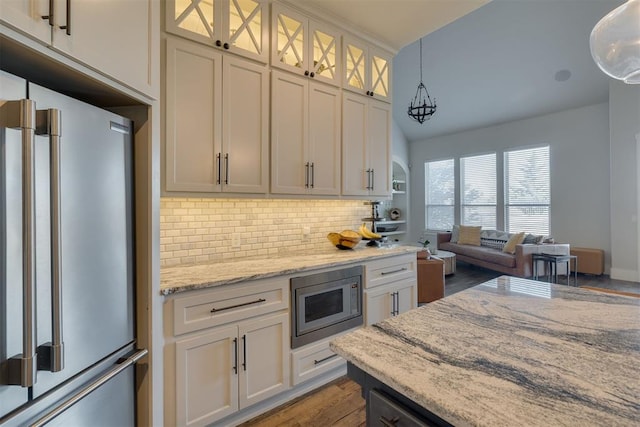 kitchen featuring light stone countertops, stainless steel appliances, glass insert cabinets, decorative light fixtures, and backsplash