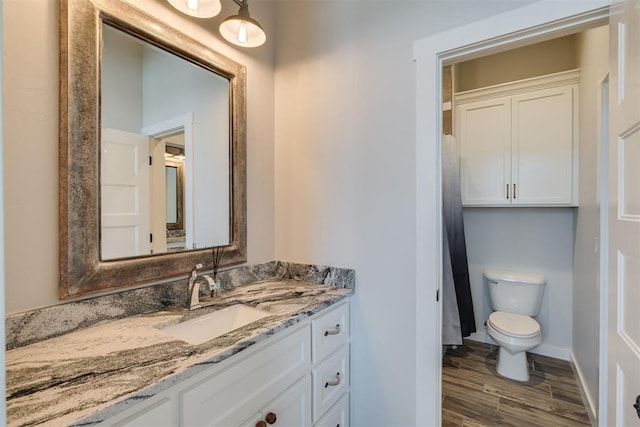 bathroom featuring baseboards, toilet, wood finished floors, and vanity