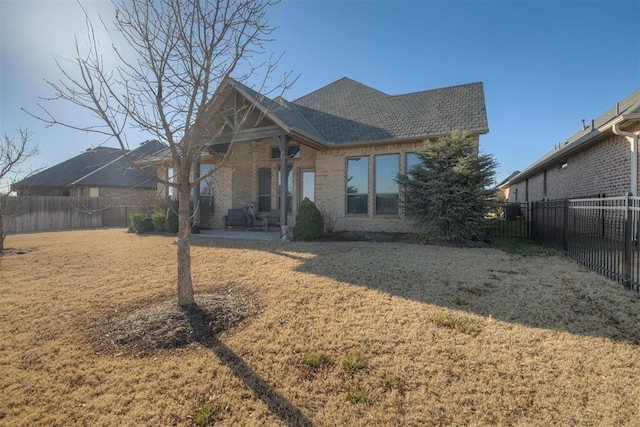 back of house with a lawn, a fenced backyard, a shingled roof, brick siding, and a patio area