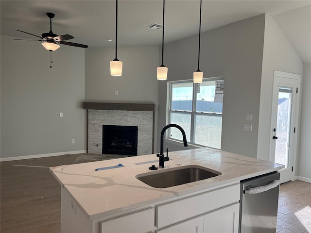 kitchen with light stone counters, a fireplace, stainless steel dishwasher, open floor plan, and a sink