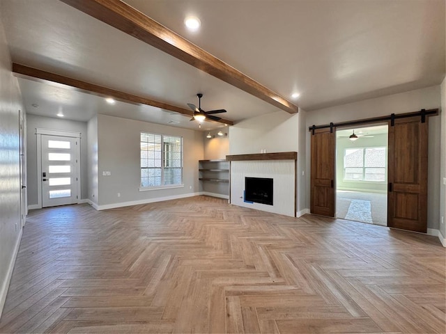 unfurnished living room featuring beam ceiling, a healthy amount of sunlight, baseboards, and a barn door