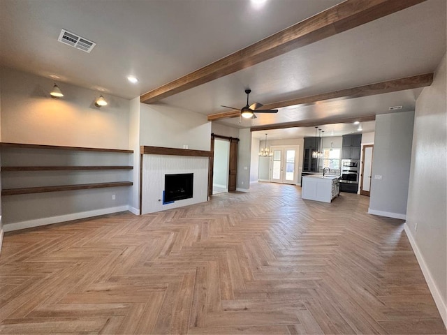 unfurnished living room featuring beam ceiling, visible vents, a sink, baseboards, and ceiling fan with notable chandelier