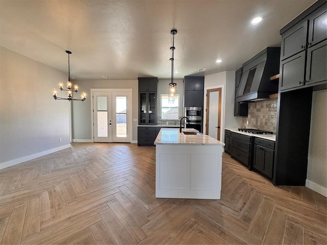 kitchen with a kitchen island with sink, stainless steel appliances, baseboards, backsplash, and custom exhaust hood