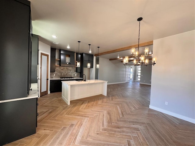 kitchen featuring a sink, light countertops, tasteful backsplash, an island with sink, and decorative light fixtures