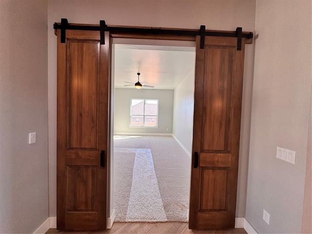 hallway with light colored carpet, baseboards, and a barn door