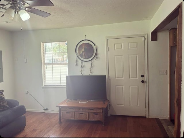 living area with dark wood-style floors, a ceiling fan, a textured ceiling, electric panel, and baseboards