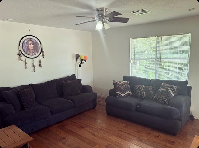 living area with a textured ceiling, ceiling fan, visible vents, baseboards, and dark wood finished floors