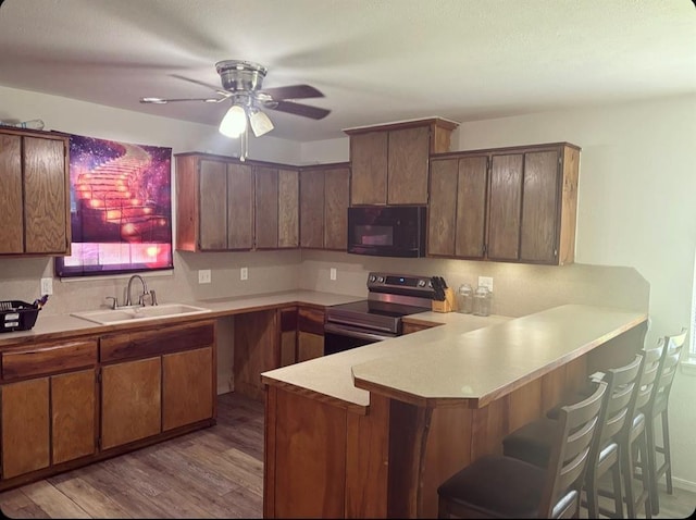 kitchen featuring light countertops, electric range, a sink, black microwave, and a peninsula