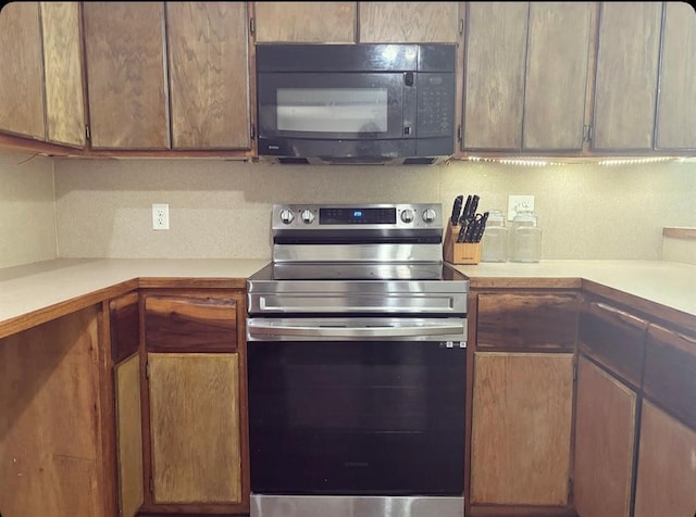 kitchen with brown cabinets, black microwave, light countertops, and electric range