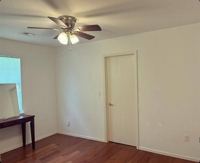 unfurnished room with dark wood-style floors, baseboards, visible vents, and ceiling fan