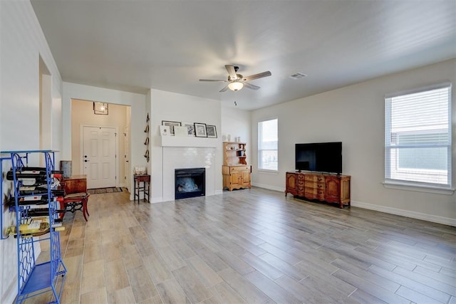 living room with ceiling fan, visible vents, baseboards, light wood-type flooring, and a glass covered fireplace