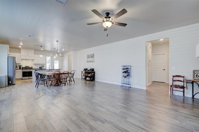 dining space featuring baseboards, visible vents, light wood finished floors, and ceiling fan with notable chandelier