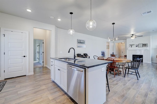 kitchen featuring visible vents, stainless steel dishwasher, a kitchen island with sink, a sink, and white cabinetry