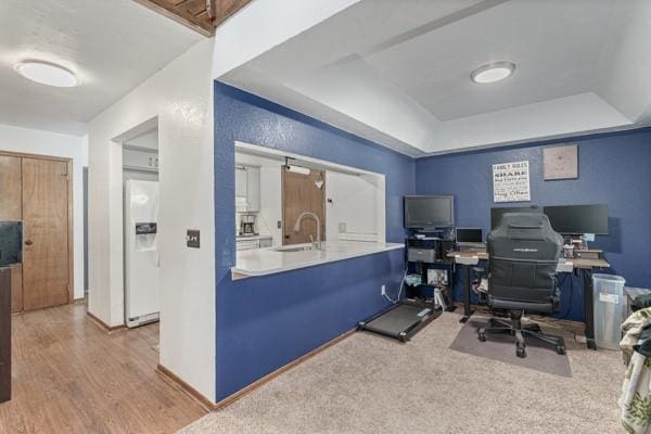 home office with a raised ceiling, a sink, baseboards, and wood finished floors