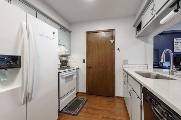 kitchen with under cabinet range hood, white appliances, wood finished floors, a sink, and light countertops