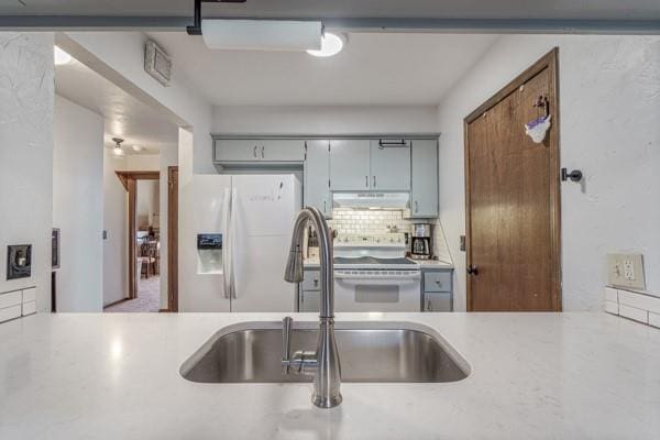 kitchen featuring white appliances, under cabinet range hood, light countertops, and a sink