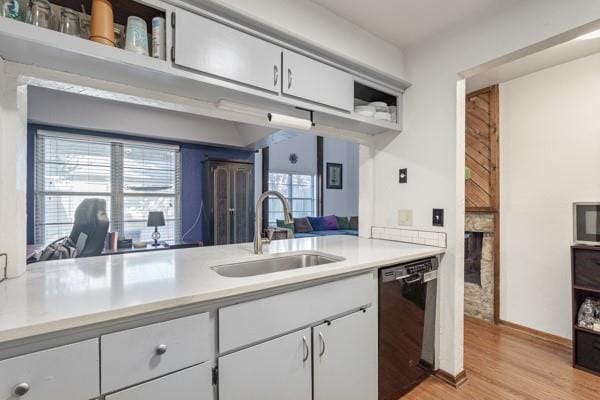 kitchen featuring light wood finished floors, black dishwasher, light countertops, and a sink