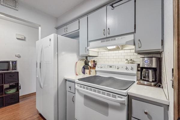 kitchen featuring white appliances, tasteful backsplash, gray cabinets, light countertops, and under cabinet range hood