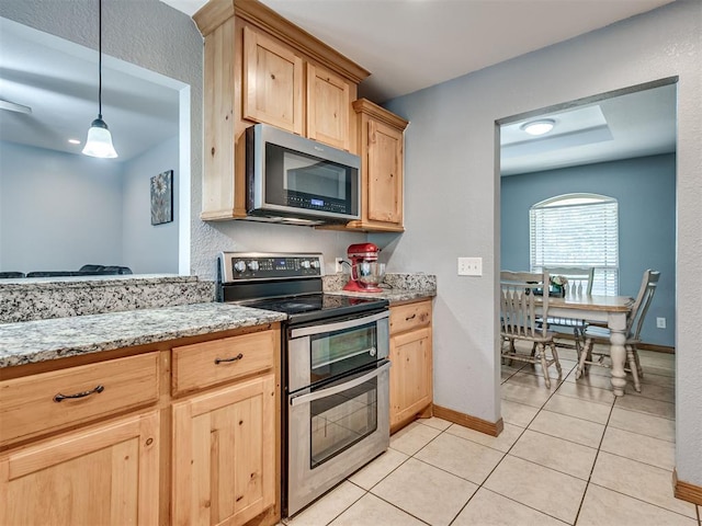 kitchen with appliances with stainless steel finishes, light tile patterned flooring, hanging light fixtures, and light brown cabinetry