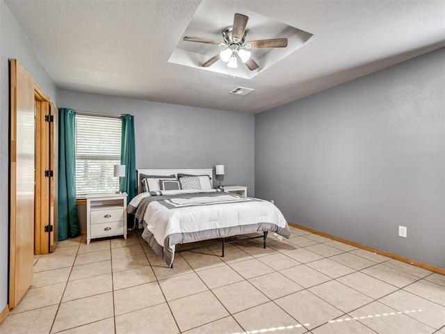 bedroom with a textured ceiling, light tile patterned flooring, visible vents, baseboards, and a tray ceiling