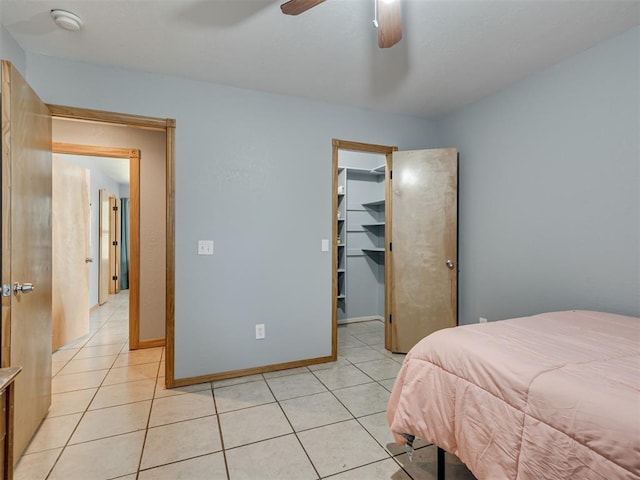 bedroom with light tile patterned floors, ceiling fan, a walk in closet, and baseboards