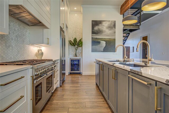 1212 W Wilshire Blvd, Nichols Hills, OK 73116 - kitchen featuring range with two ovens, custom range hood, beverage cooler, wood finished floors, and tasteful backsplash