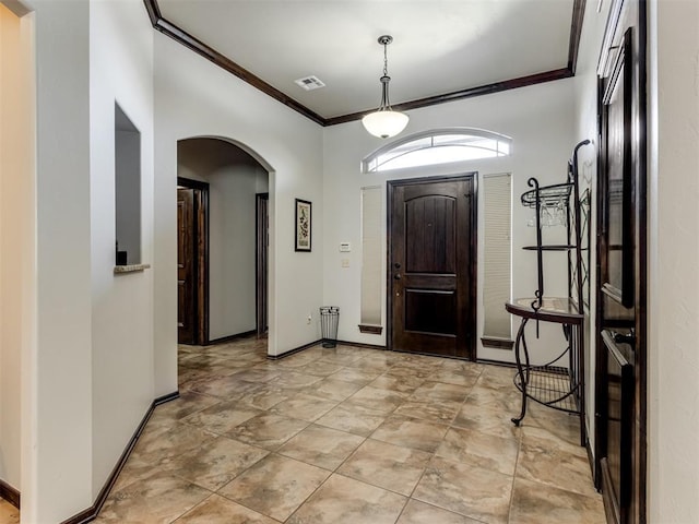 foyer entrance featuring arched walkways, baseboards, visible vents, and crown molding