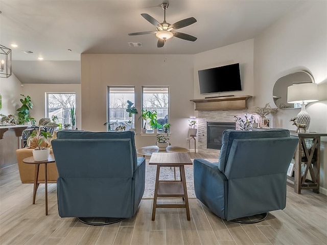 living room with a ceiling fan, wood tiled floor, visible vents, and a glass covered fireplace