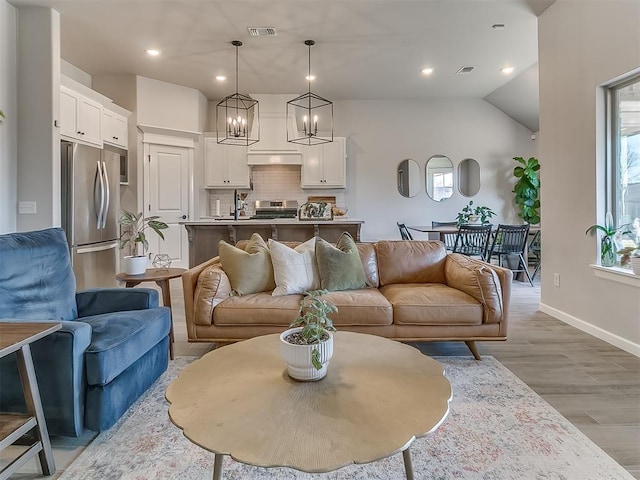 living area featuring visible vents, vaulted ceiling, light wood-style flooring, and baseboards