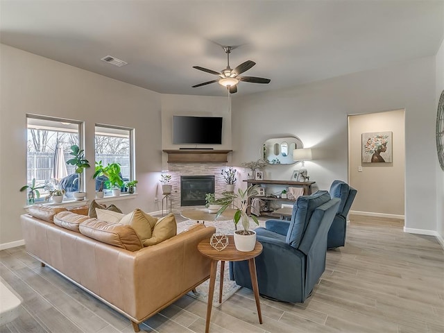 living area featuring light wood-style flooring, visible vents, ceiling fan, and a stone fireplace