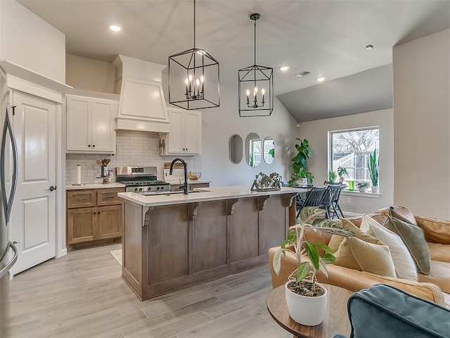 kitchen featuring light countertops, a center island with sink, white cabinetry, and pendant lighting