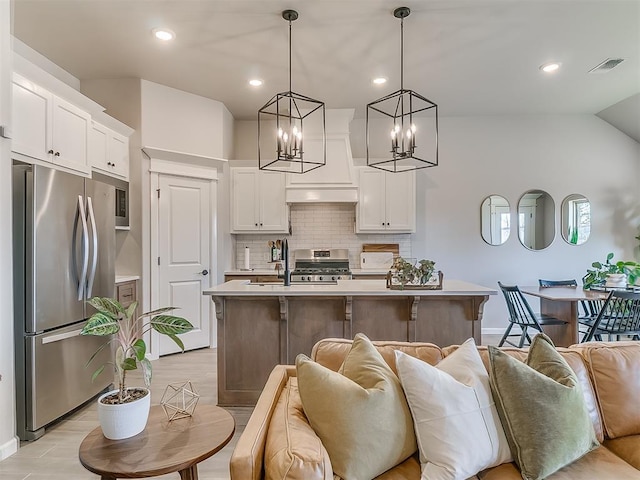 kitchen with decorative light fixtures, a center island with sink, light countertops, appliances with stainless steel finishes, and white cabinetry